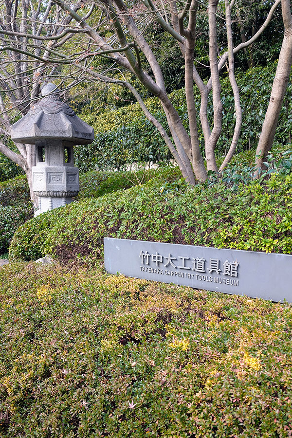 Entrance sign for the Takenaka Carpentry Tools Museum surrounded by greenery and a traditional Japanese stone lantern in Kobe, Japan
