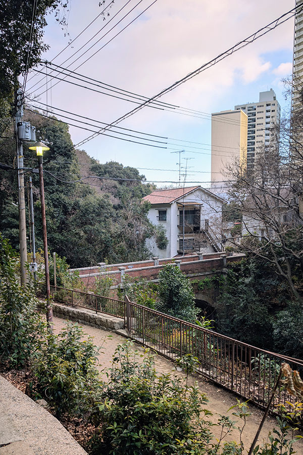 View of Isago-bashi Bridge near Shin-Kobe Station, a historic stone arch bridge surrounded by greenery with city buildings in the background