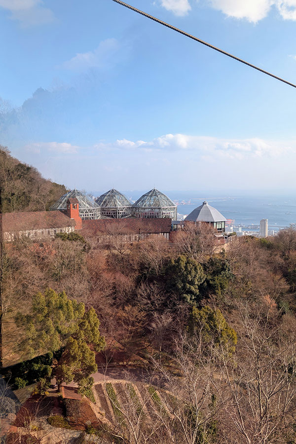 Overhead view of Kobe Nunobiki Herb Gardens with glass greenhouses nestled in the mountains, overlooking Osaka Bay