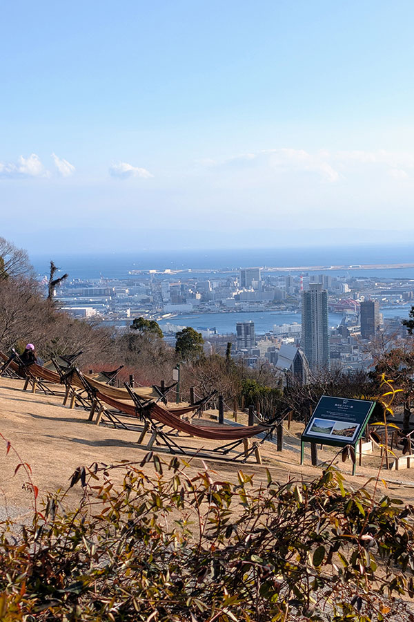 View from Wind Hill Grass Square (Kaze-no-Oka) in Kobe with wooden hammocks facing the city skyline and harbor below