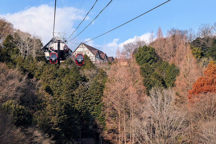 Gondolas arriving at the upper station of the Kobe Nunobiki Ropeway with forested hills and a half-timbered mountain lodge in the background