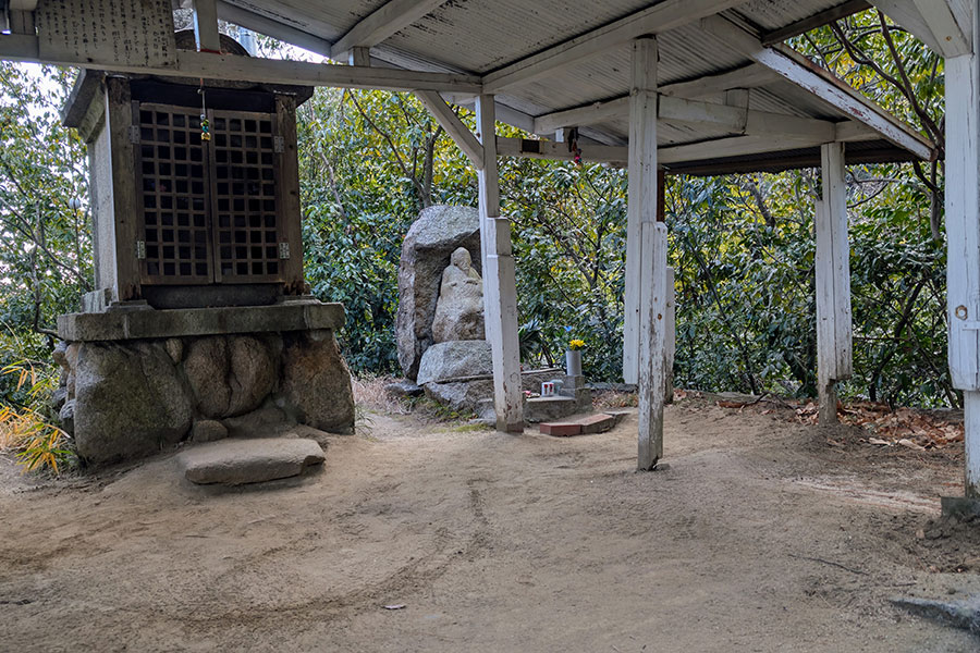 Small shrine along the Nunobiki Falls hiking trail in Kobe, Japan, with a stone statue and wooden shelter surrounded by forest