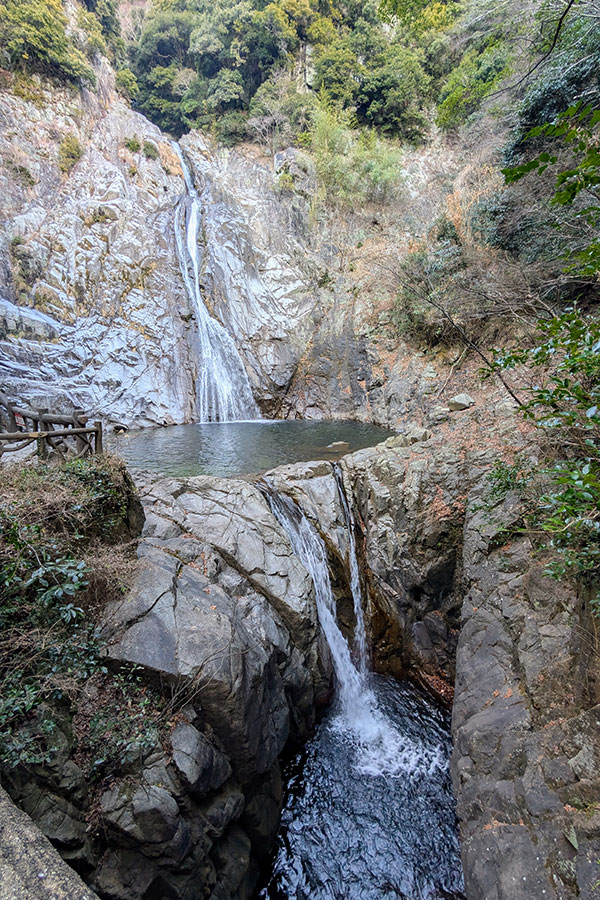 On-taki Waterfall in Kobe, Japan, with a powerful multi-tiered cascade flowing into a rocky gorge surrounded by forest