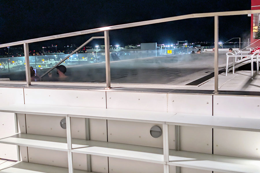 Steam rising from the rooftop infinity pool at the TWA Hotel, with the lights of JFK Airport visible in the background at night.