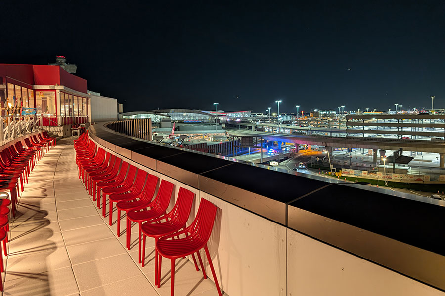 The unique experience of the TWA Hotel's rooftop bar at night, offering guests close-up views of planes and airport operations from behind a row of vibrant red seating