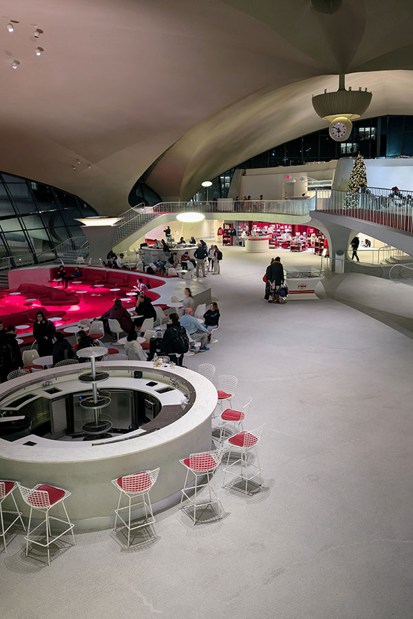 Guests enjoying drinks in the TWA Hotel's sunken lounge, with its distinctive red seating and central bar area.
