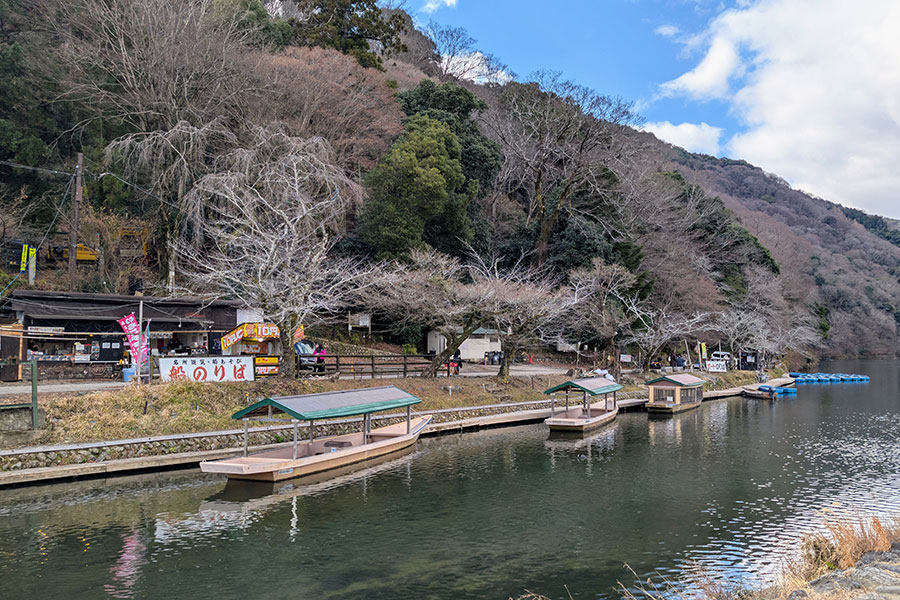 Traditional flat-bottomed boats moored along the Oigawa River in Arashiyama, Kyoto, with the bare trees of the surrounding mountains visible in the background, a scenic view for a travel blog on outdoor activities in Japan.