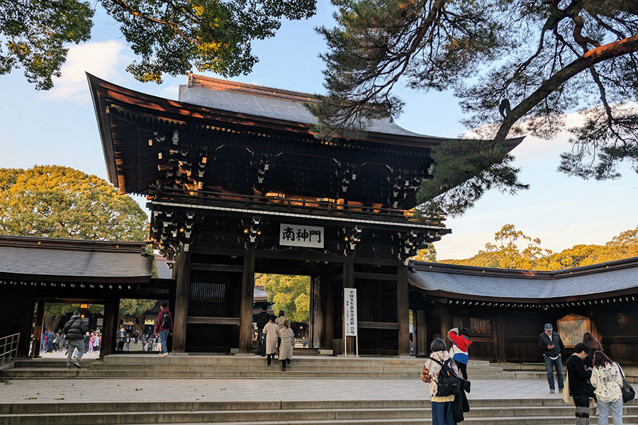 Grand wooden torii gate leading into Meiji Jingu Shrine in Tokyo, with people walking around the entrance on a clear day, ideal for a travel blog exploring spiritual sites in Japan.