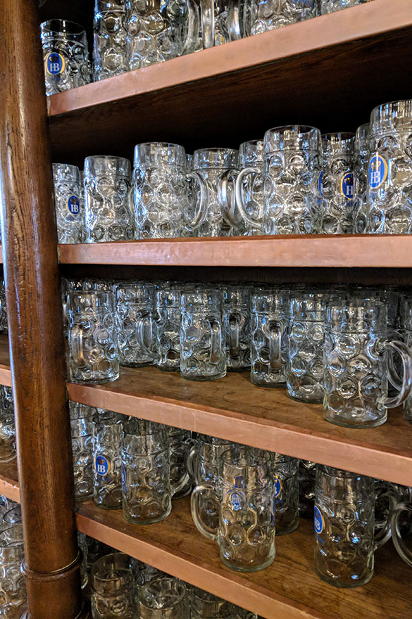 Shelves filled with traditional glass beer mugs, or steins, with the blue HB logo at the Hofbräuhaus in Munich.