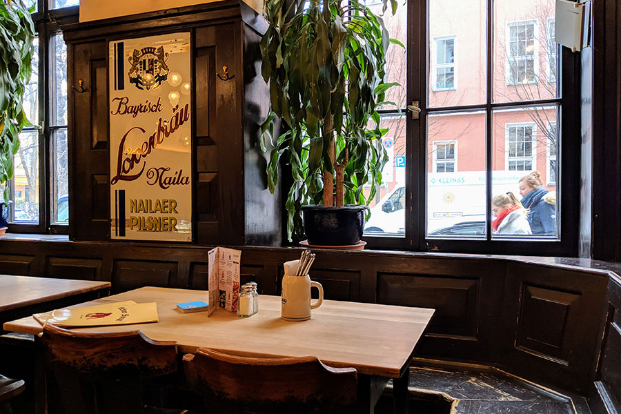 The traditional, dark wood-paneled interior of a Munich Wirtshaus, with a table set for dining next to a large window.
