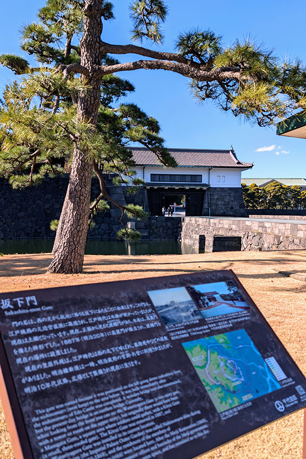 An informational sign with a map explaining the history of the Sakashita-mon Gate at the Tokyo Imperial Palace, which is visible in the background.