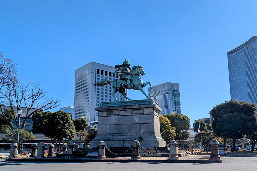 A bronze statue of samurai Kusunoki Masashige on horseback in the outer gardens of the Tokyo Imperial Palace, with modern skyscrapers in the background.
