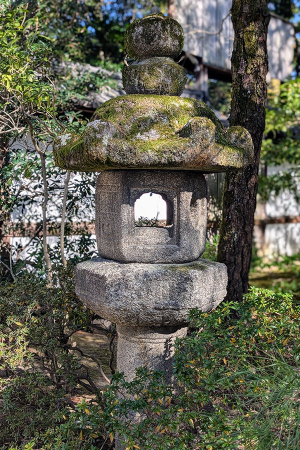 A traditional Japanese stone lantern, or tōrō, covered with green moss in the tranquil gardens of the Kyoto Imperial Palace.