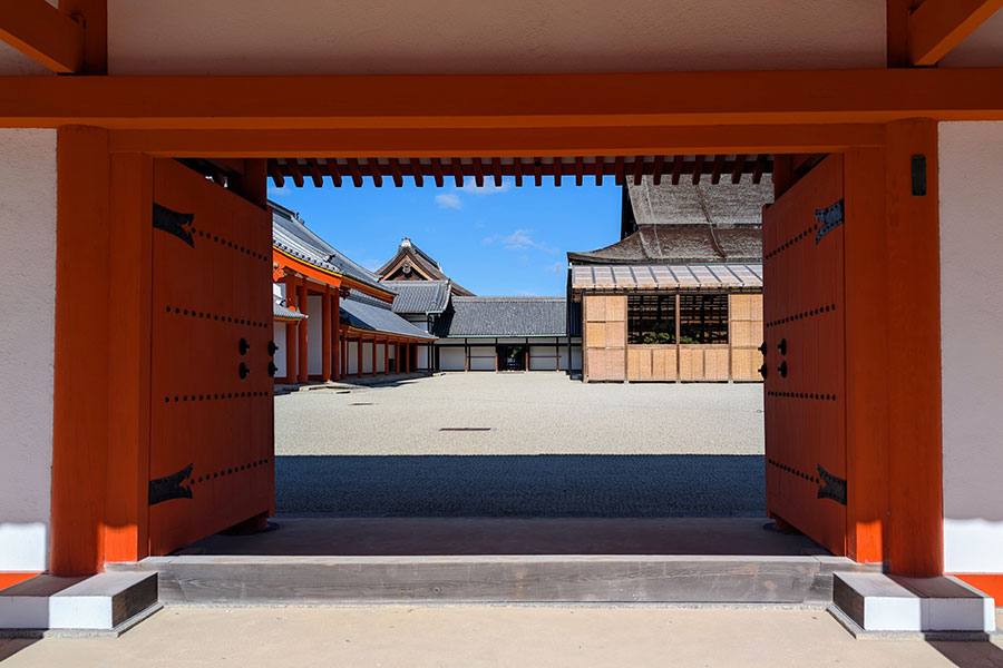 A view through the open, bright orange doors of the Jomeimon Gate into a white gravel courtyard at the Kyoto Imperial Palace.