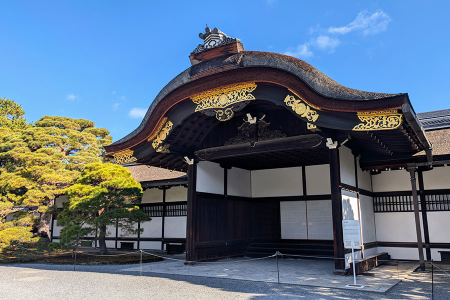 The Okurumayose entrance for official visitors at the Kyoto Imperial Palace, featuring a traditional curved cypress bark roof and ornate gold details.