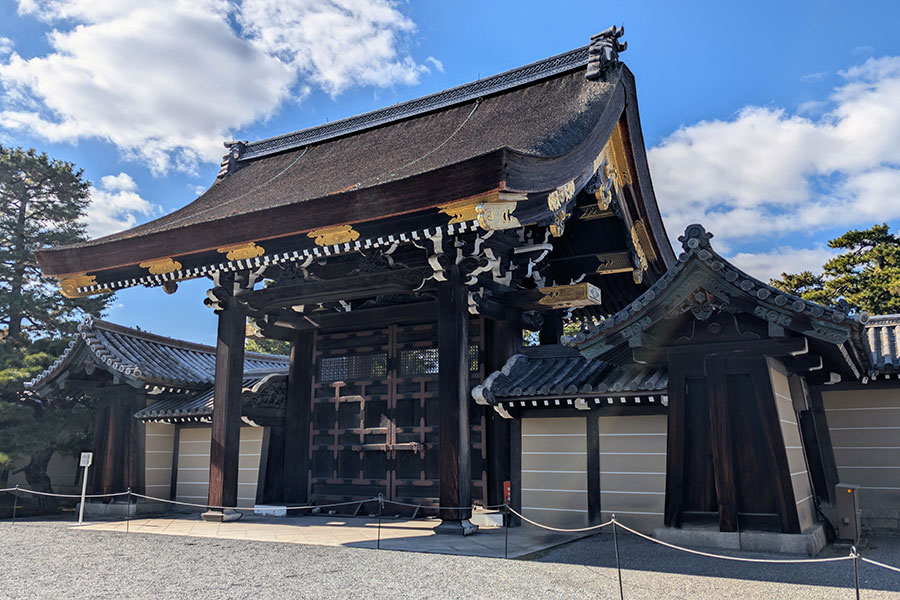 The grand Sakuheimon Gate at the Kyoto Imperial Palace, an imposing dark wood structure with a massive cypress bark roof.