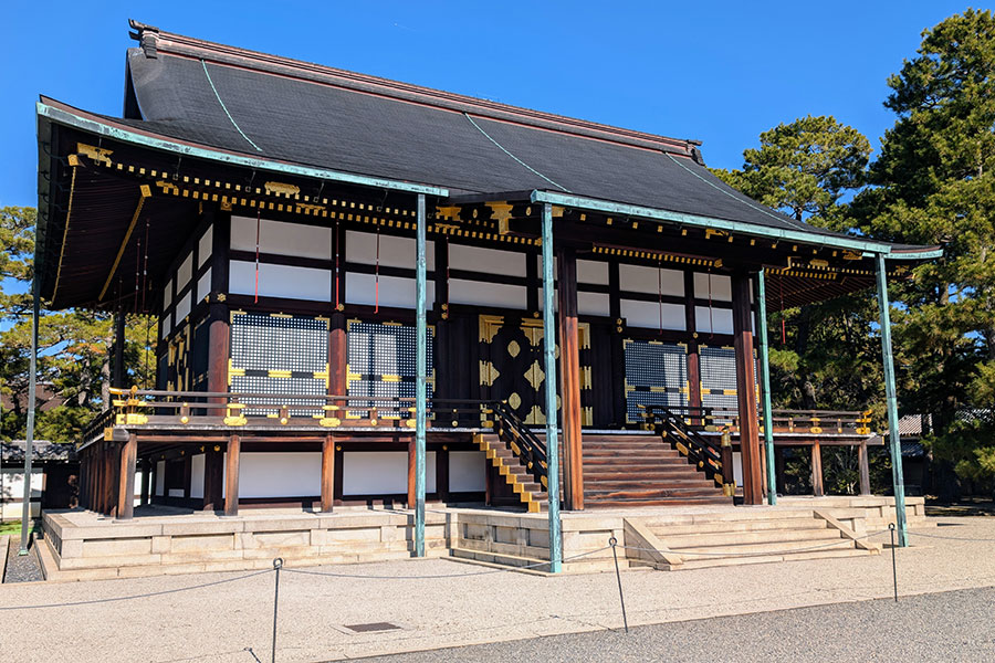 The elegant Shunkoden Hall at the Kyoto Imperial Palace, a building featuring a dark roof, black lacquer woodwork, white walls, and ornate gold metal details.