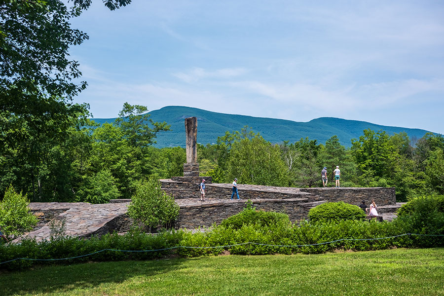 Visitors exploring the massive bluestone ramps and central monolith of Harvey Fite's Opus 40 sculpture park in Saugerties, NY, with the Catskill Mountains in the background.
