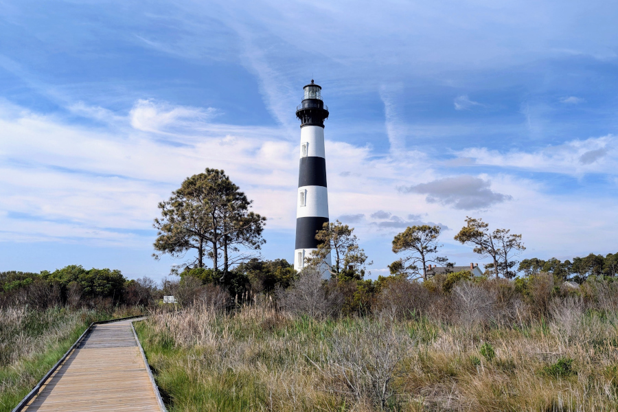 Bodie Island Lighthouse in the Outer Banks of North Carolina, with its black-and-white striped tower rising above marshland and a wooden boardwalk leading toward it.