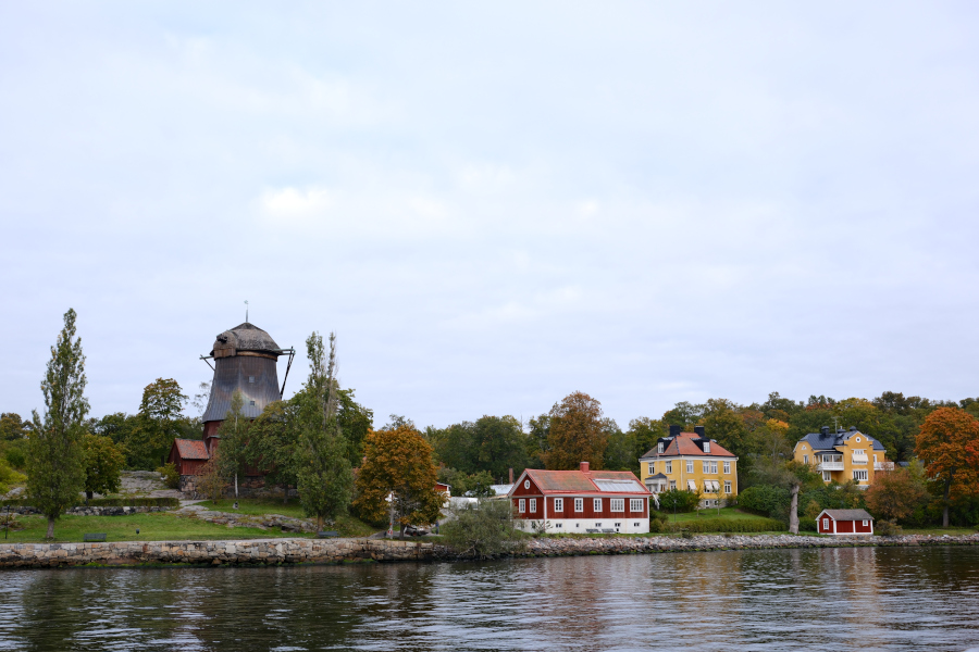 A historic wooden windmill and traditional red and yellow Swedish houses along the waterfront at Prins Eugens Waldemarsudde in Stockholm during October.