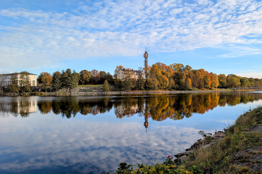 Vibrant autumn trees and the Kaknästornet tower reflecting in the still blue waters of the Djurgårdsbrunnskanalen in Stockholm.