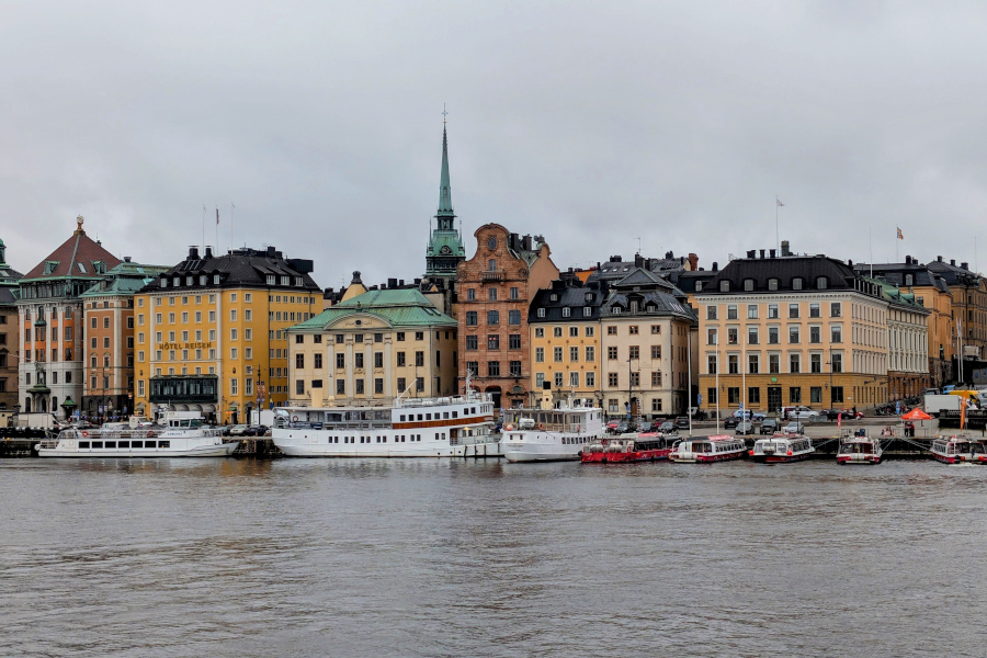 Traditional white passenger ferries and classic architecture along the Skeppsbron waterfront, including the yellow facade of the historic Hotel Reisen.