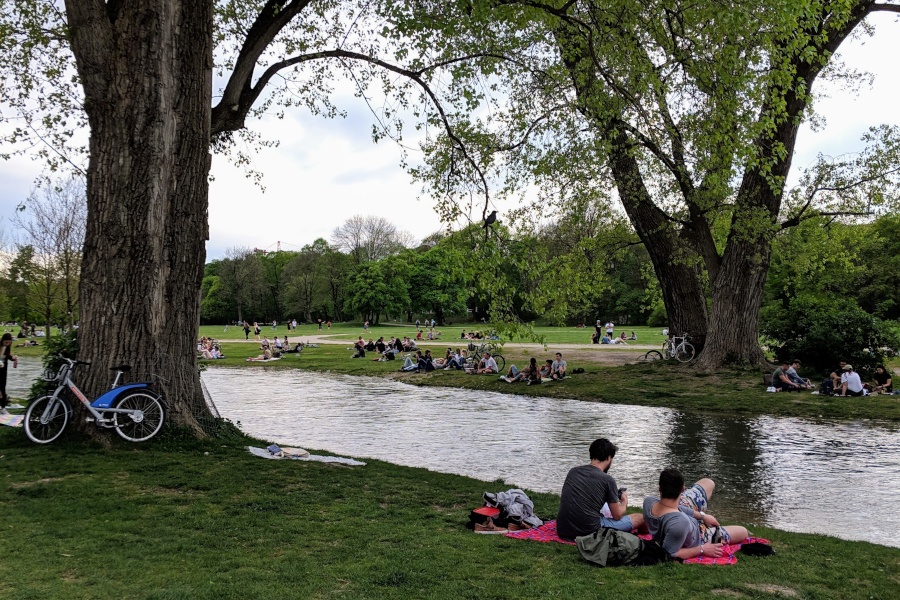 People relaxing and picnicking along the banks of the Eisbach stream in Munich's English Garden.