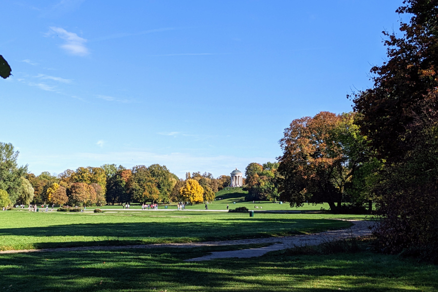 Wide view of the green lawn and Monopteros temple atop a hill in Englischer Garten, Munich.