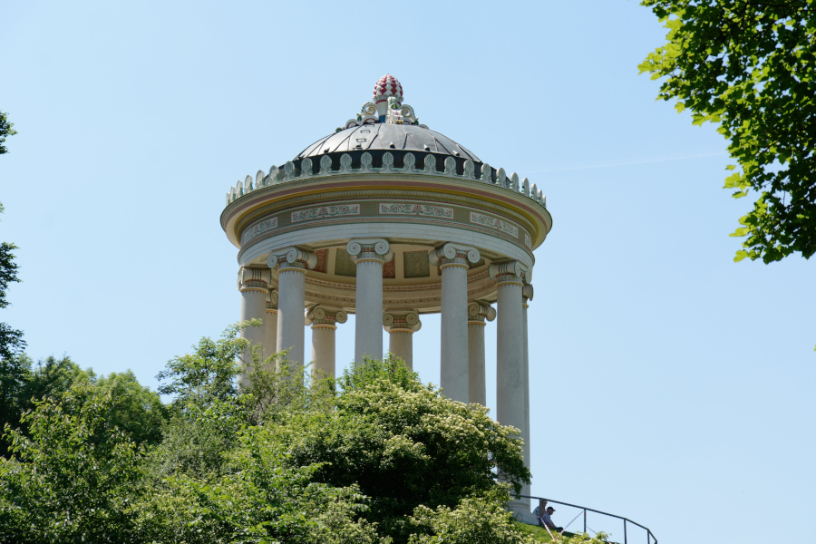 Greek-style Monopteros temple pavilion rising above green trees in the English Garden, Munich.